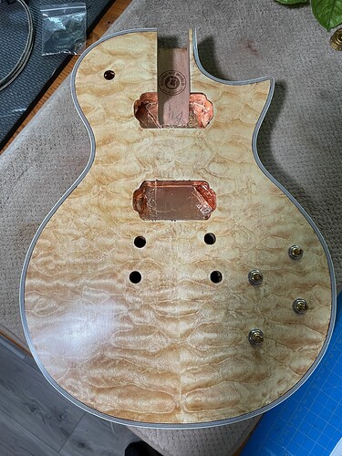 The guitar body before finishing, showing the quilted maple veneer and copper foil in the pickup routes